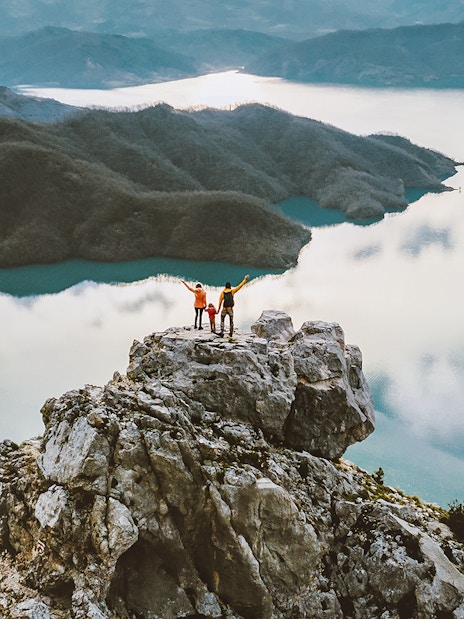 Family hiking on Gamti mountain summit with lake and hills in the background.