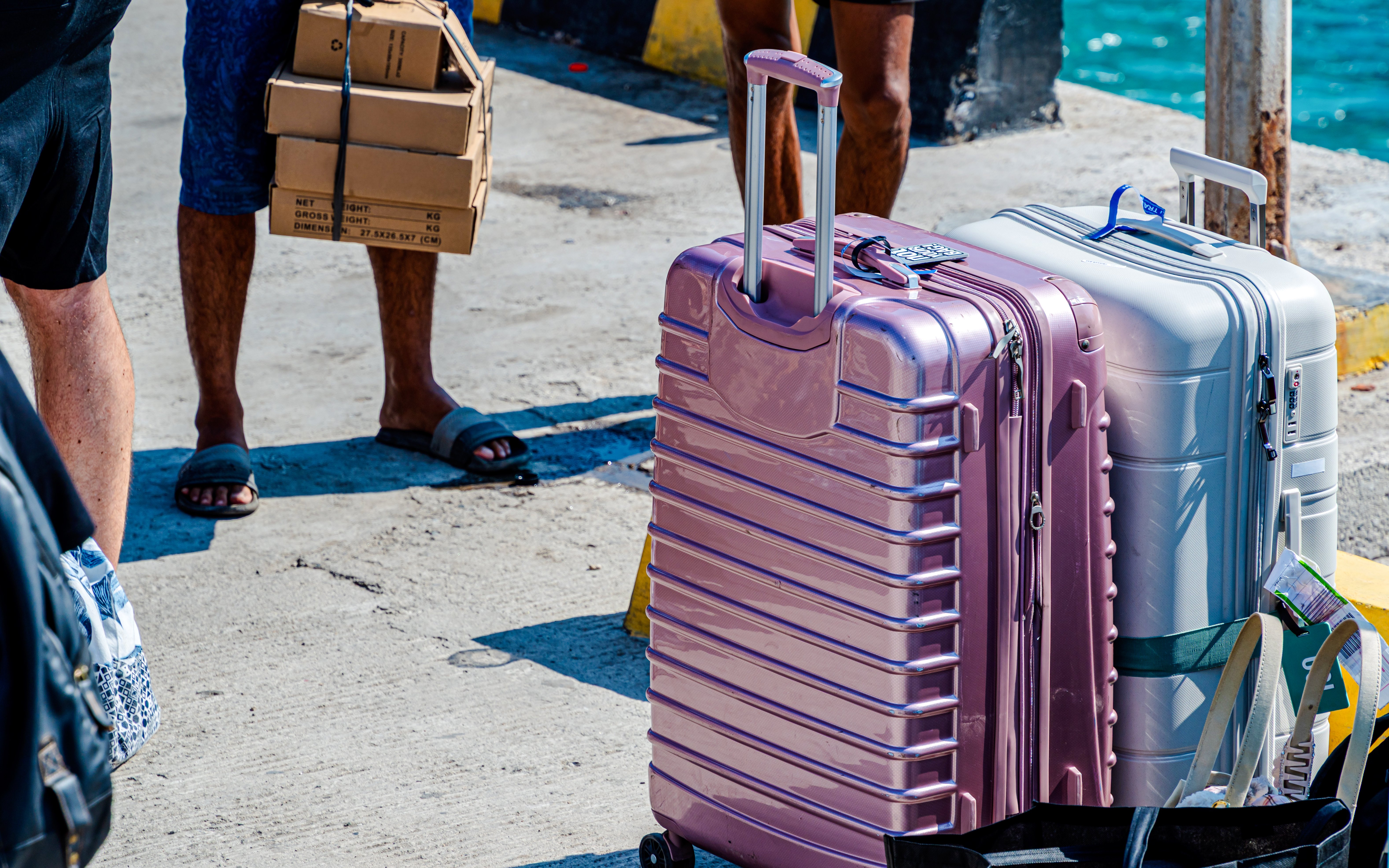 Suitcases and cardboard boxes on concrete near water.