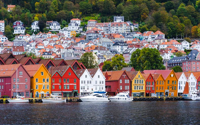 Colorful wooden houses along the waterfront in Bergen, Norway, with hillside homes in the background.
