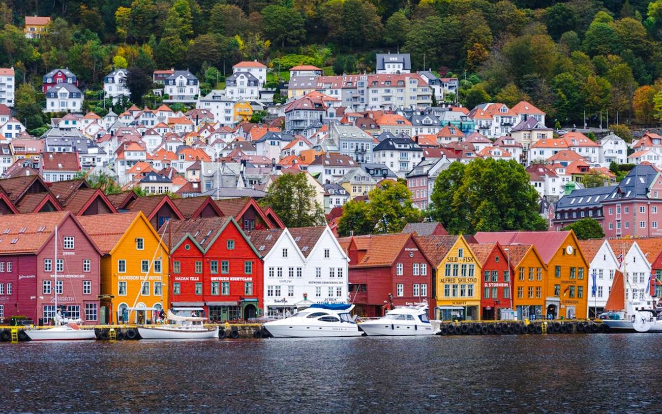 Colorful wooden houses along the waterfront in Bergen, Norway, with hillside homes in the background.
