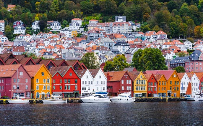 Colorful wooden houses along the waterfront in Bergen, Norway, with hillside homes in the background.