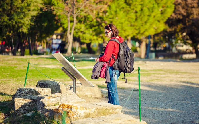 Tourist with audio guide reading sign at archeological site.