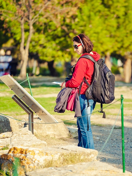 Tourist with audio guide reading sign at archeological site.