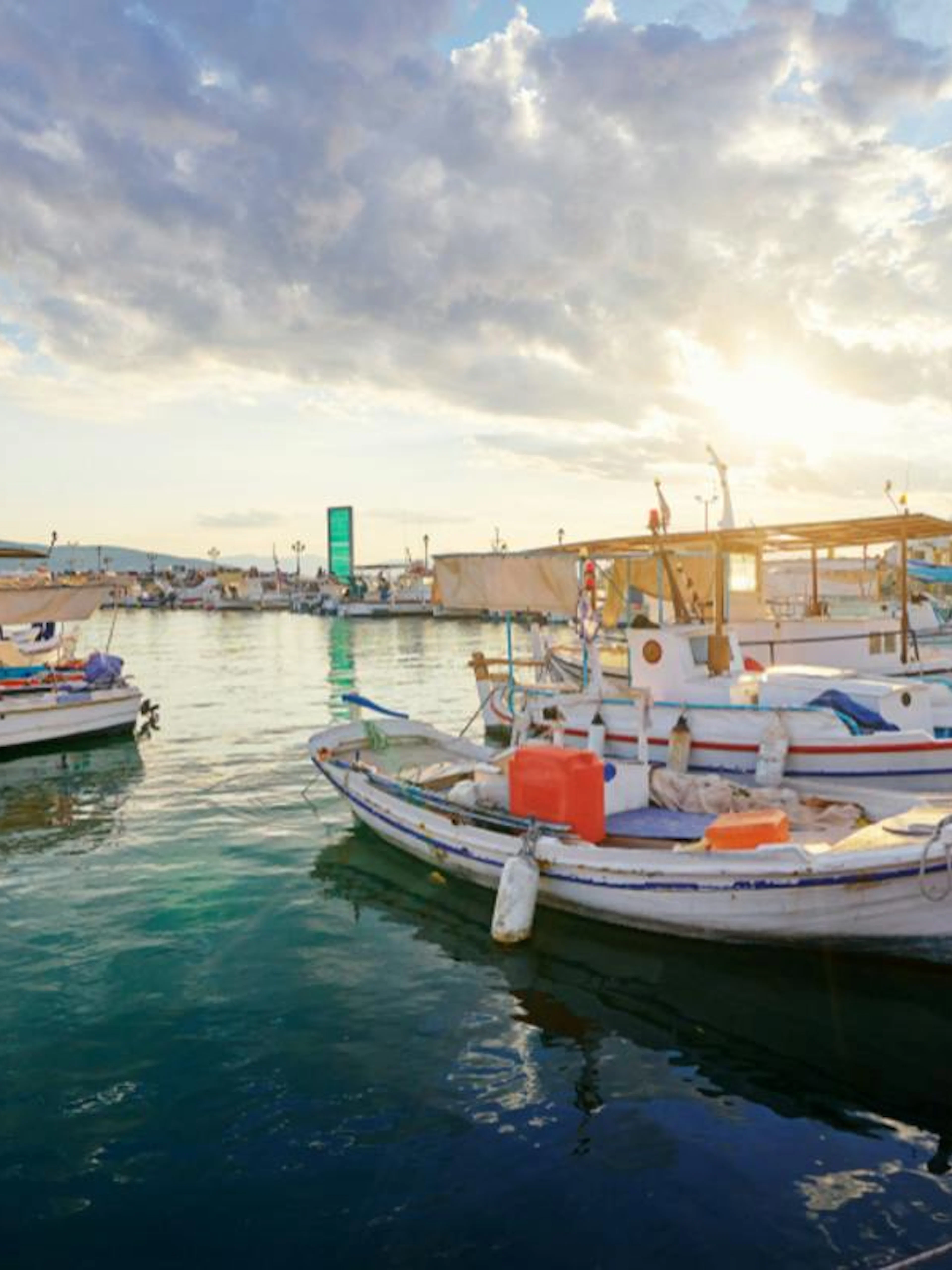 Boats docked at a pier in Aegina, Greece, with a sunset over the water.