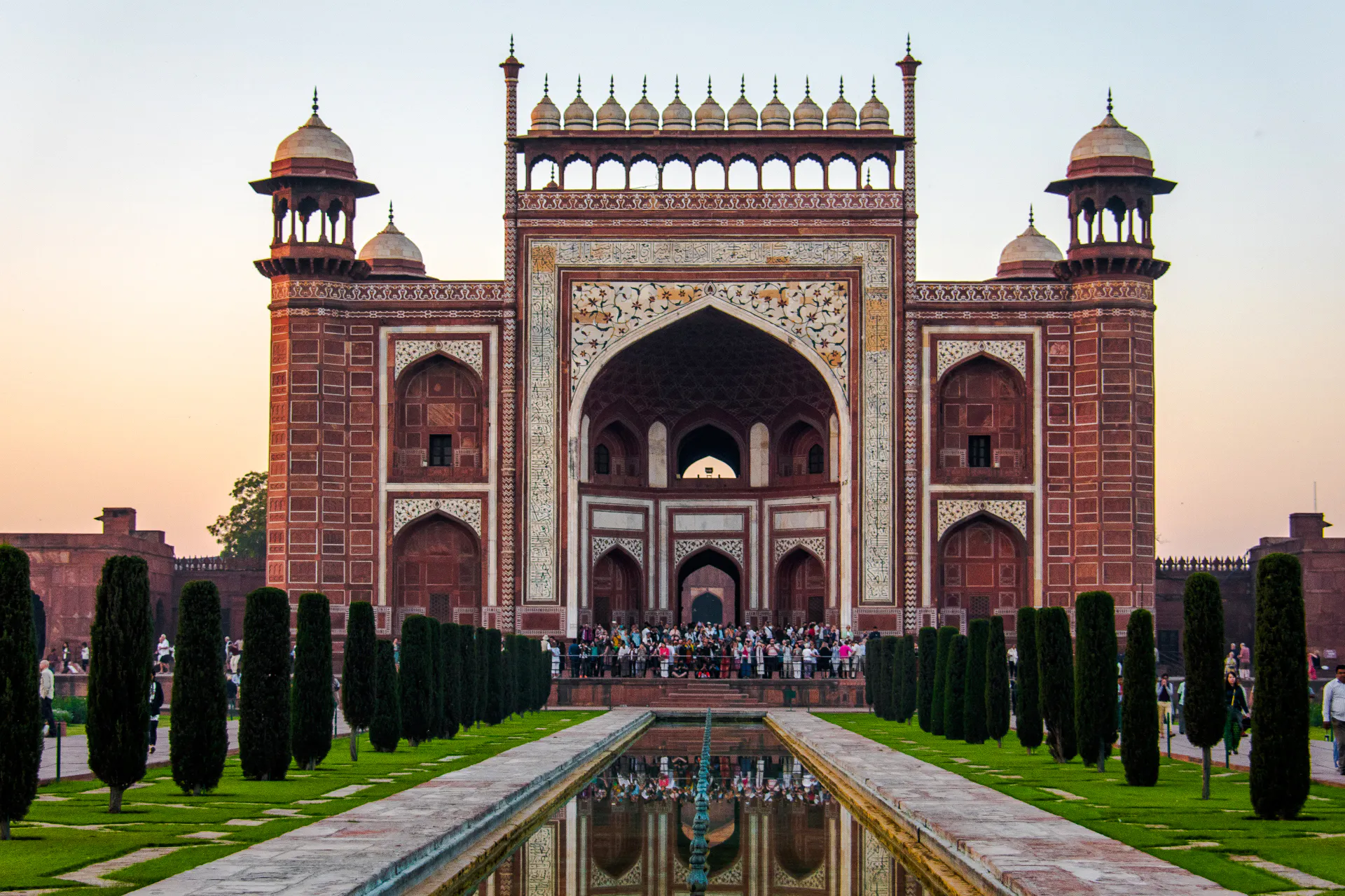 Entrance gate of the Taj Mahal complex at sunrise, Agra, with tourists gathered.