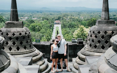 Couple standing at Borobudur Temple with lush landscape in the background.