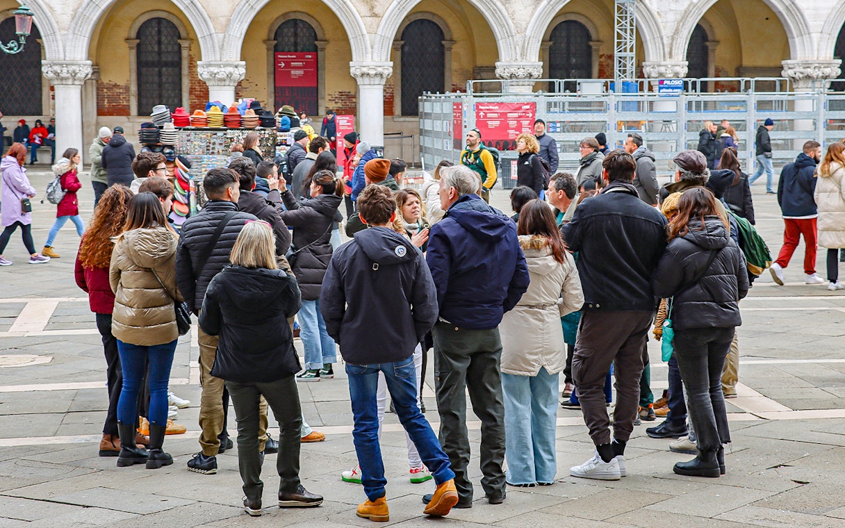 Tour group gathered in a Venetian square, listening to a guide near historic arches.