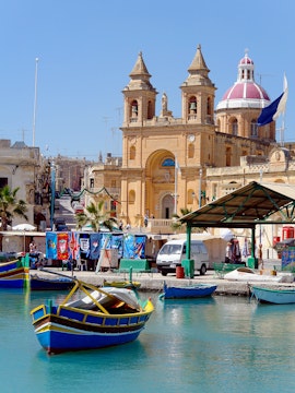 Traditional Maltese boat in harbor near church, Blue Grotto Tours, Malta.
