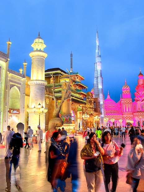 Tourists walking through Global Village Dubai with illuminated pavilions and cultural architecture.