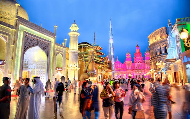Tourists walking through Global Village Dubai with illuminated pavilions and cultural architecture.