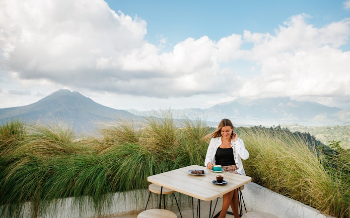 Woman enjoying coffee with Mount Batur view in Bali during sunrise jeep tour.