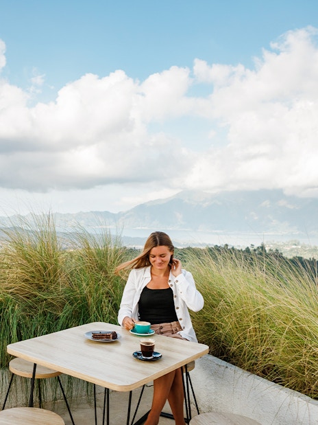Woman enjoying coffee with Mount Batur view in Bali during sunrise jeep tour.