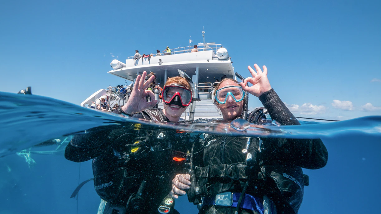 Snorkelers giving OK sign near boat at Outer Great Barrier Reef, Cairns trip.