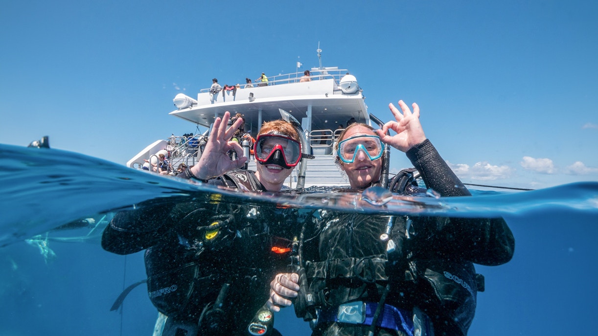Snorkelers giving OK sign near boat at Outer Great Barrier Reef, Cairns trip.