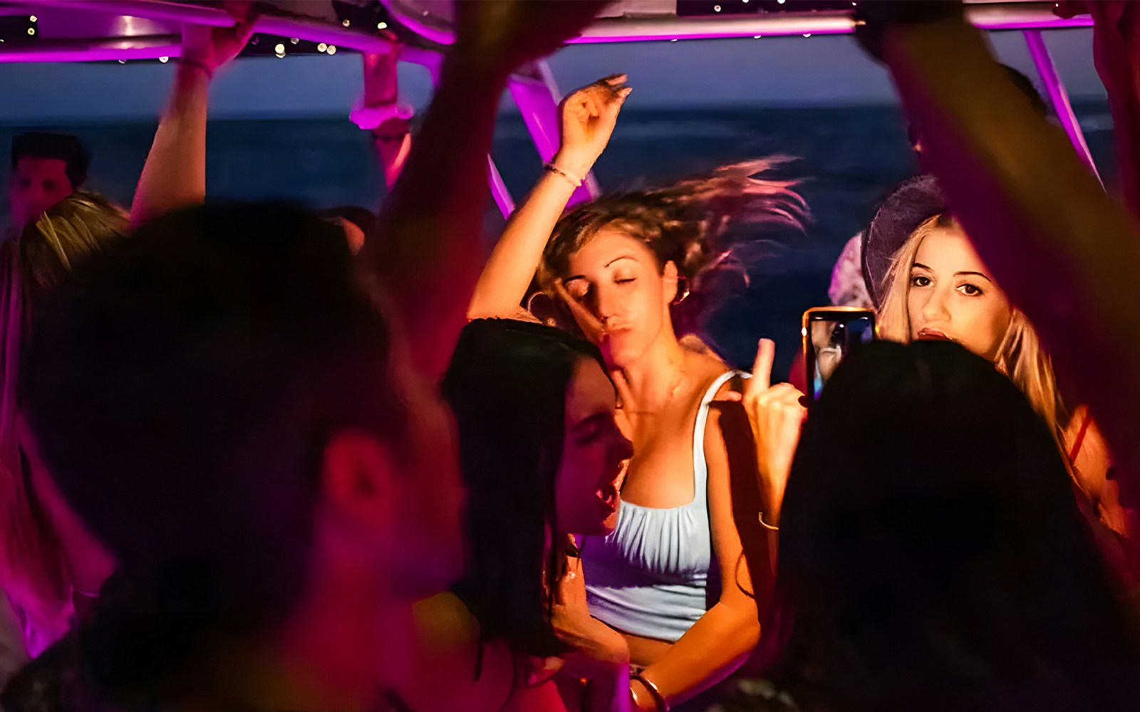 Girl dancing on Dubai Marina yacht with DJ and partygoers in background