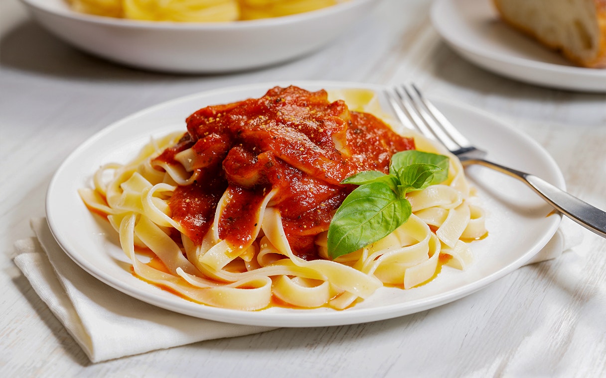 Fettuccine pasta with tomato sauce and basil on a white plate.