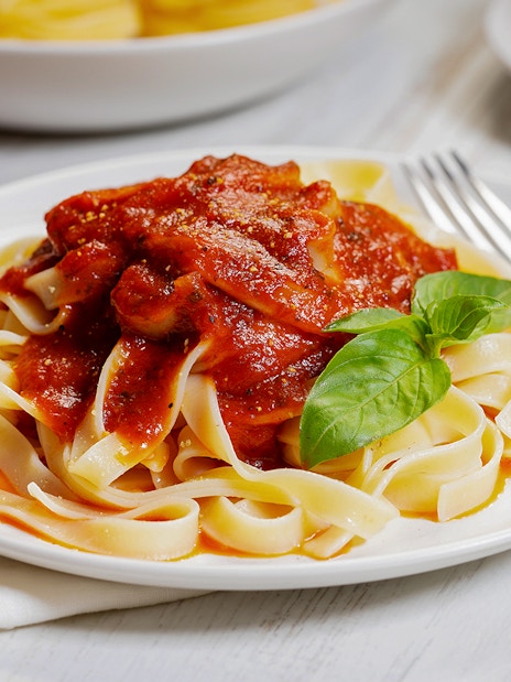 Fettuccine pasta with tomato sauce and basil on a white plate.