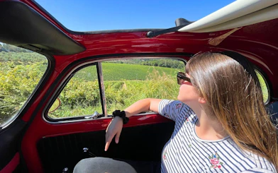 Woman enjoying vineyard view from a vintage Fiat 500 in Tuscany.