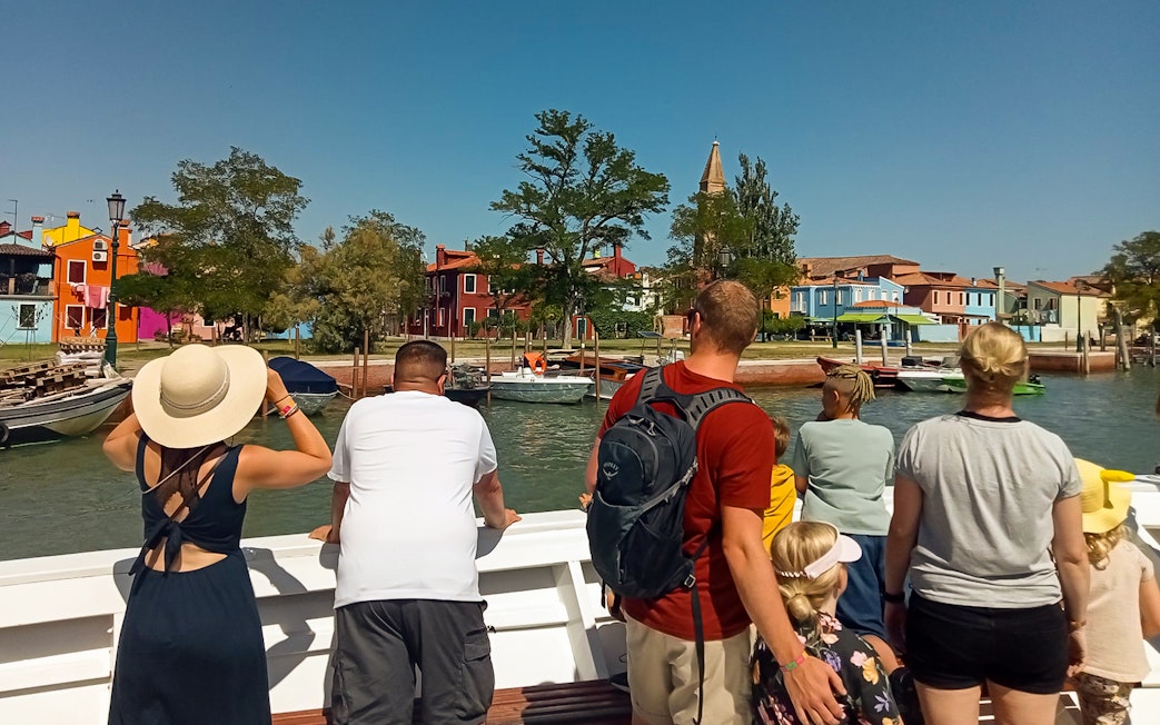 Tourists on a vaporetto viewing colorful houses on Burano Island, Venice.