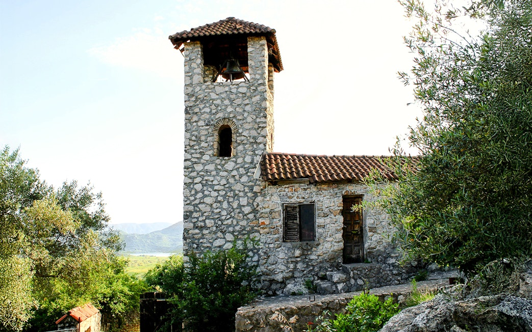Stone bell tower of the Kom Monastery, Lake Skadar, surrounded by greenery.