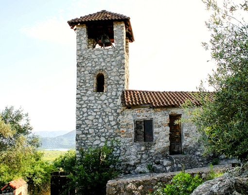 Stone bell tower of the Kom Monastery, Lake Skadar, surrounded by greenery.