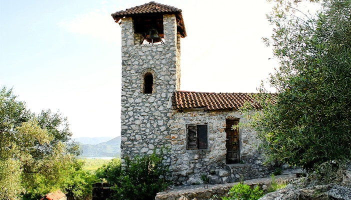 Stone bell tower of the Kom Monastery, Lake Skadar, surrounded by greenery.