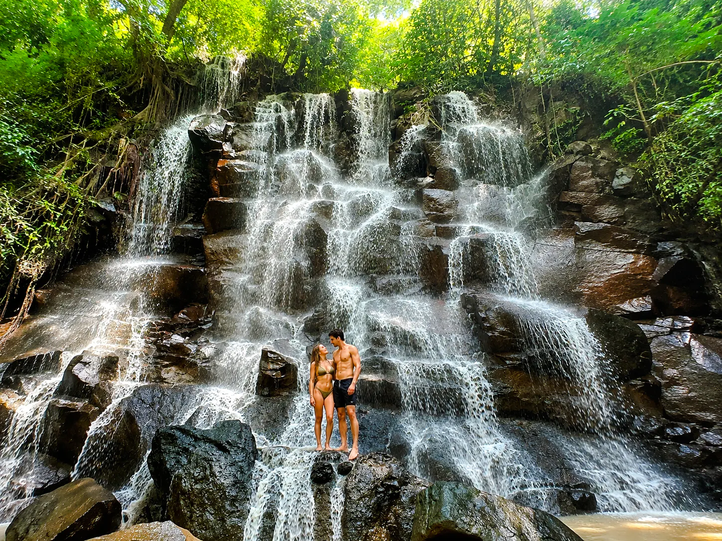 Couple standing on rocks at a waterfall in Ubud, Bali during a private tour adventure.