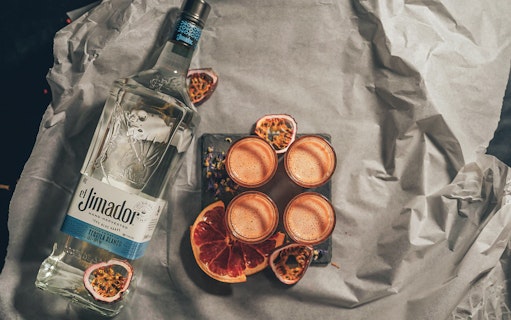 Bottle of tequila with four cocktails and sliced fruit at Neverland Bar & Escape Room.