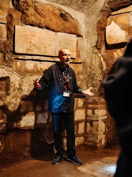 Guide explaining Roman Catacombs to tourists during Capuchin Crypts tour.