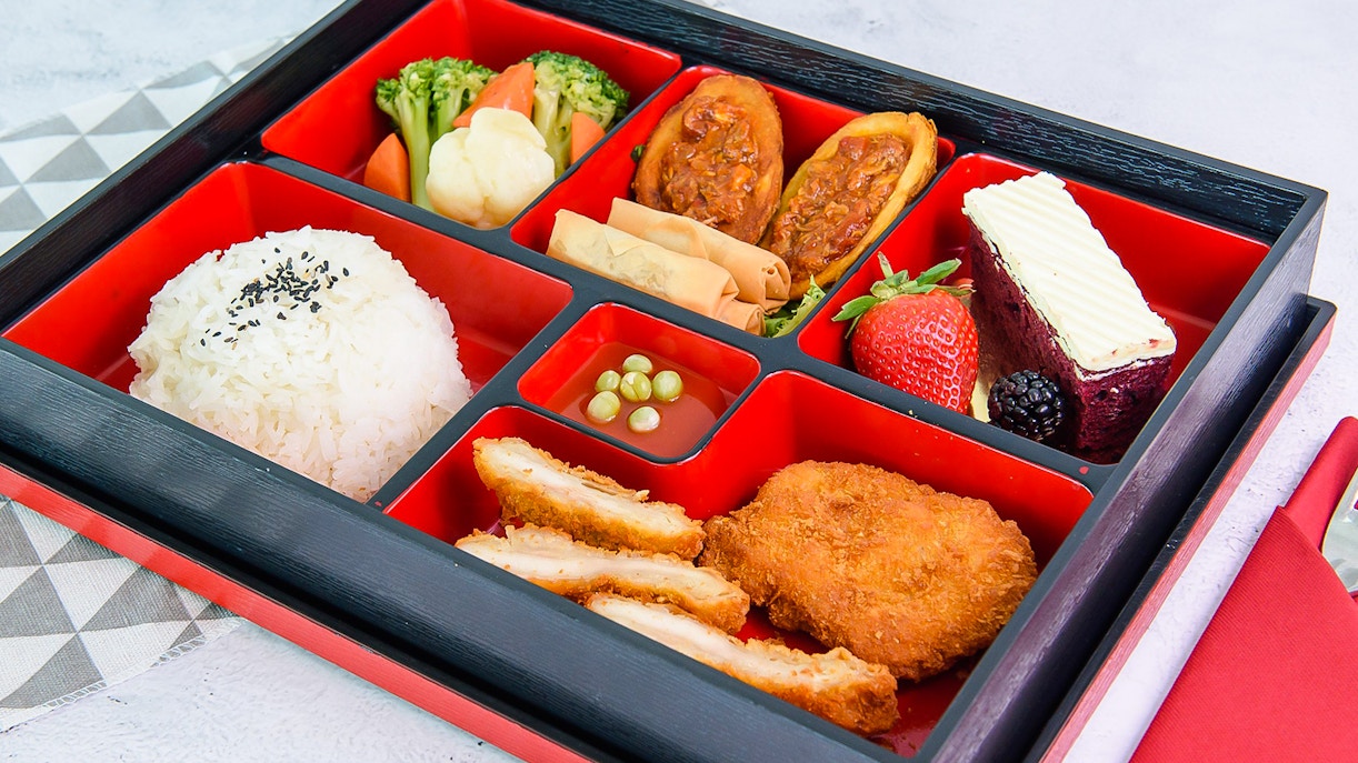 Bento box with rice, vegetables, fried chicken, spring rolls, and dessert in Singapore.