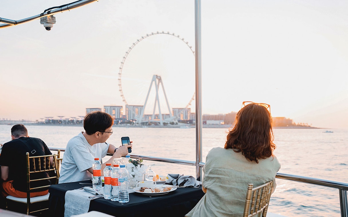 Guests dining on a sunset cruise in Dubai Marina with Ferris wheel view.