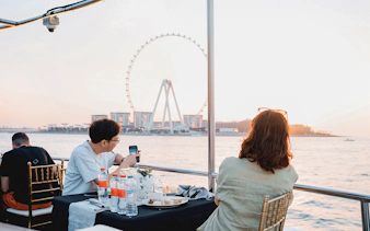 Guests dining on a sunset cruise in Dubai Marina with Ferris wheel view.