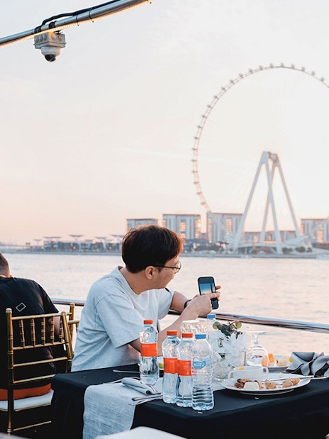 Guests dining on a sunset cruise in Dubai Marina with Ferris wheel view.