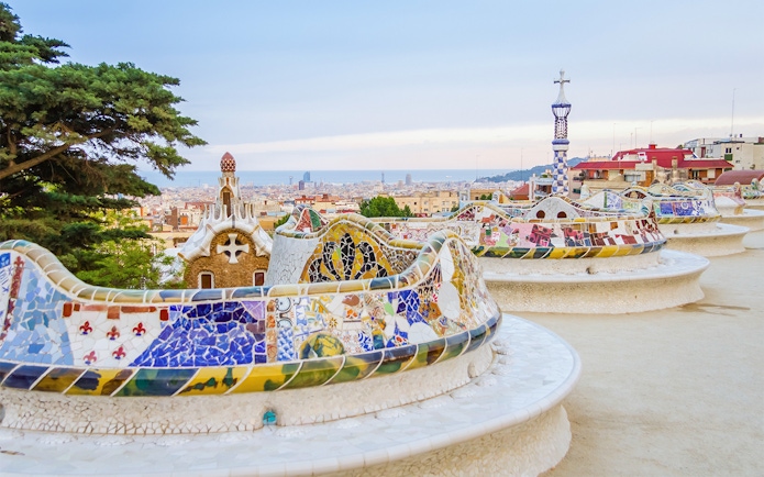 Colorful mosaic bench in Park Güell, Barcelona, with cityscape in the background.