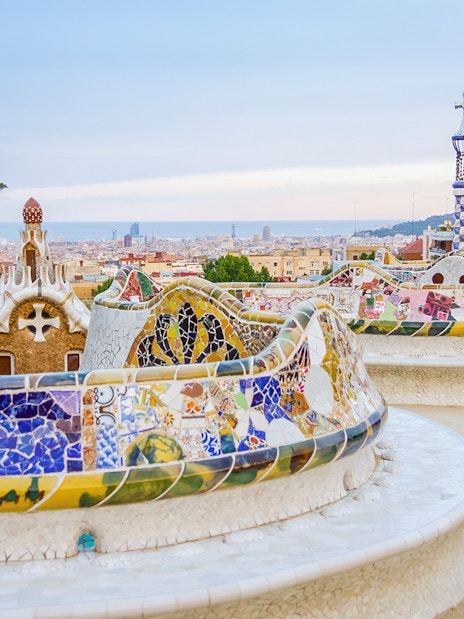 Colorful mosaic bench in Park Güell, Barcelona, with cityscape in the background.