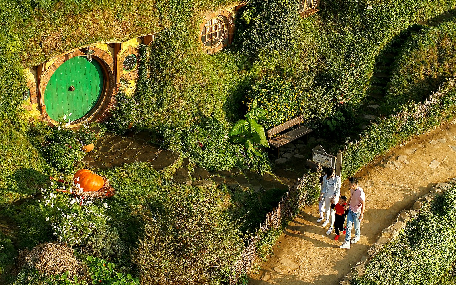 Family exploring Hobbiton Movie Set with iconic round door, lush greenery, and garden path.