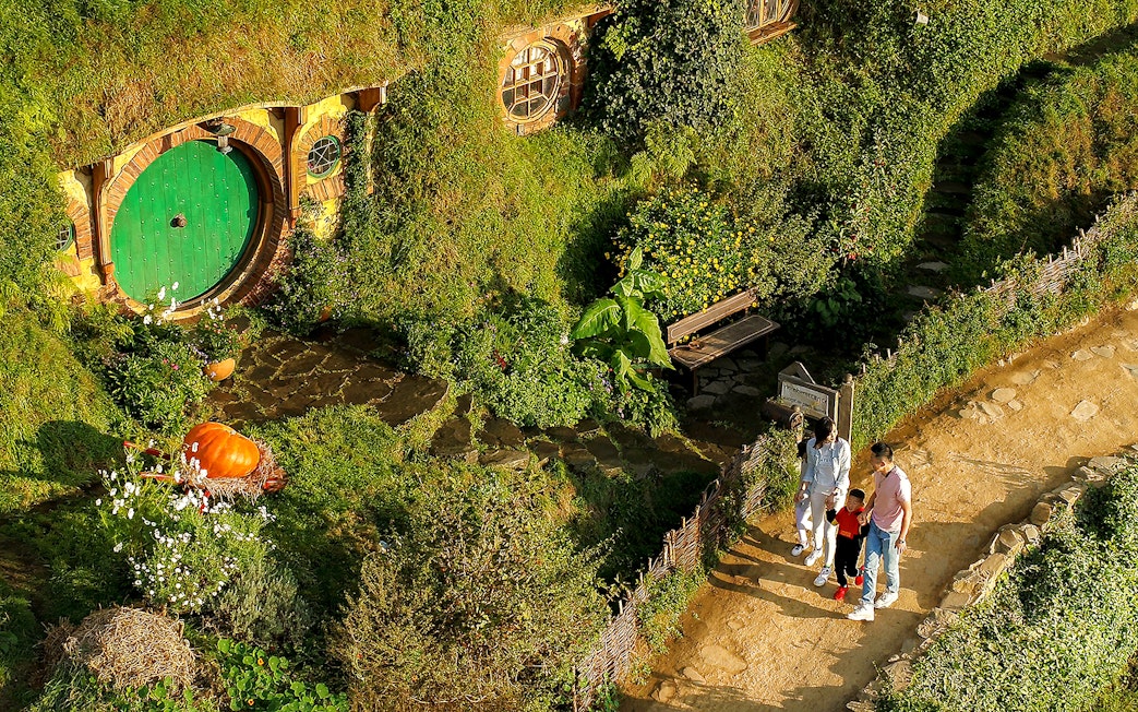 Family exploring Hobbiton Movie Set with iconic round door, lush greenery, and garden path.