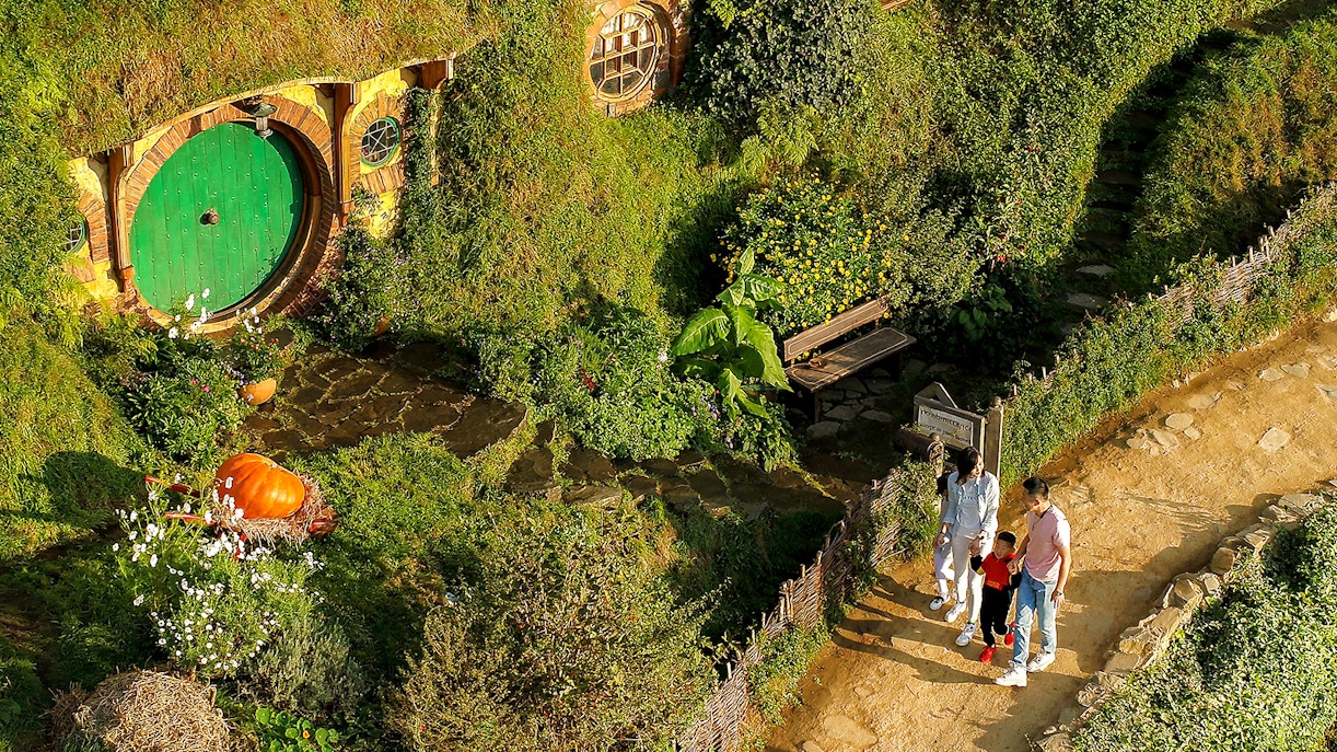 Family exploring Hobbiton Movie Set with iconic round door, lush greenery, and garden path.
