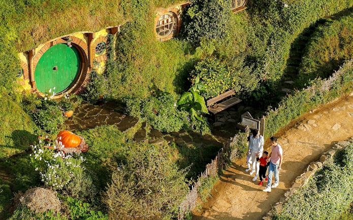 Family exploring Hobbiton Movie Set with iconic round door, lush greenery, and garden path.