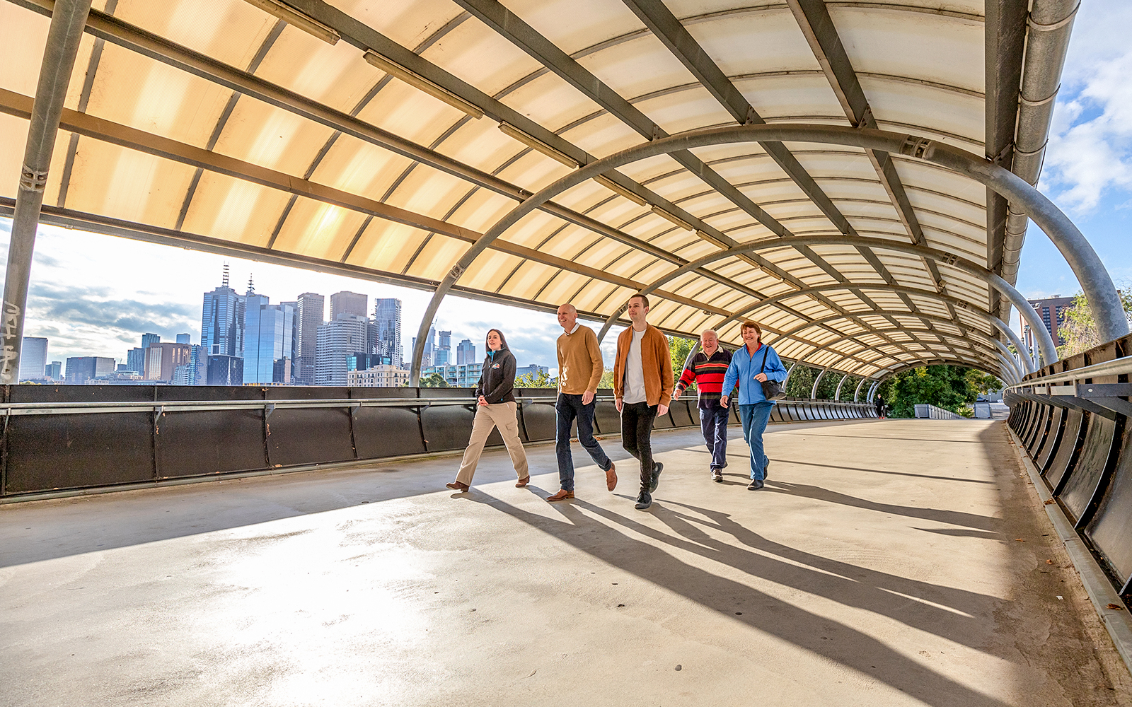 Group walking on a bridge with Melbourne skyline in the background, part of Sports Lovers Day Tour.