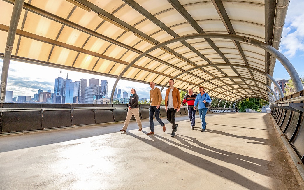 Group walking on a bridge with Melbourne skyline in the background, part of Sports Lovers Day Tour.