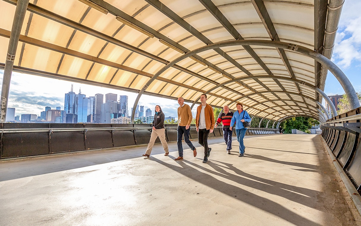 Group walking on a bridge with Melbourne skyline in the background, part of Sports Lovers Day Tour.
