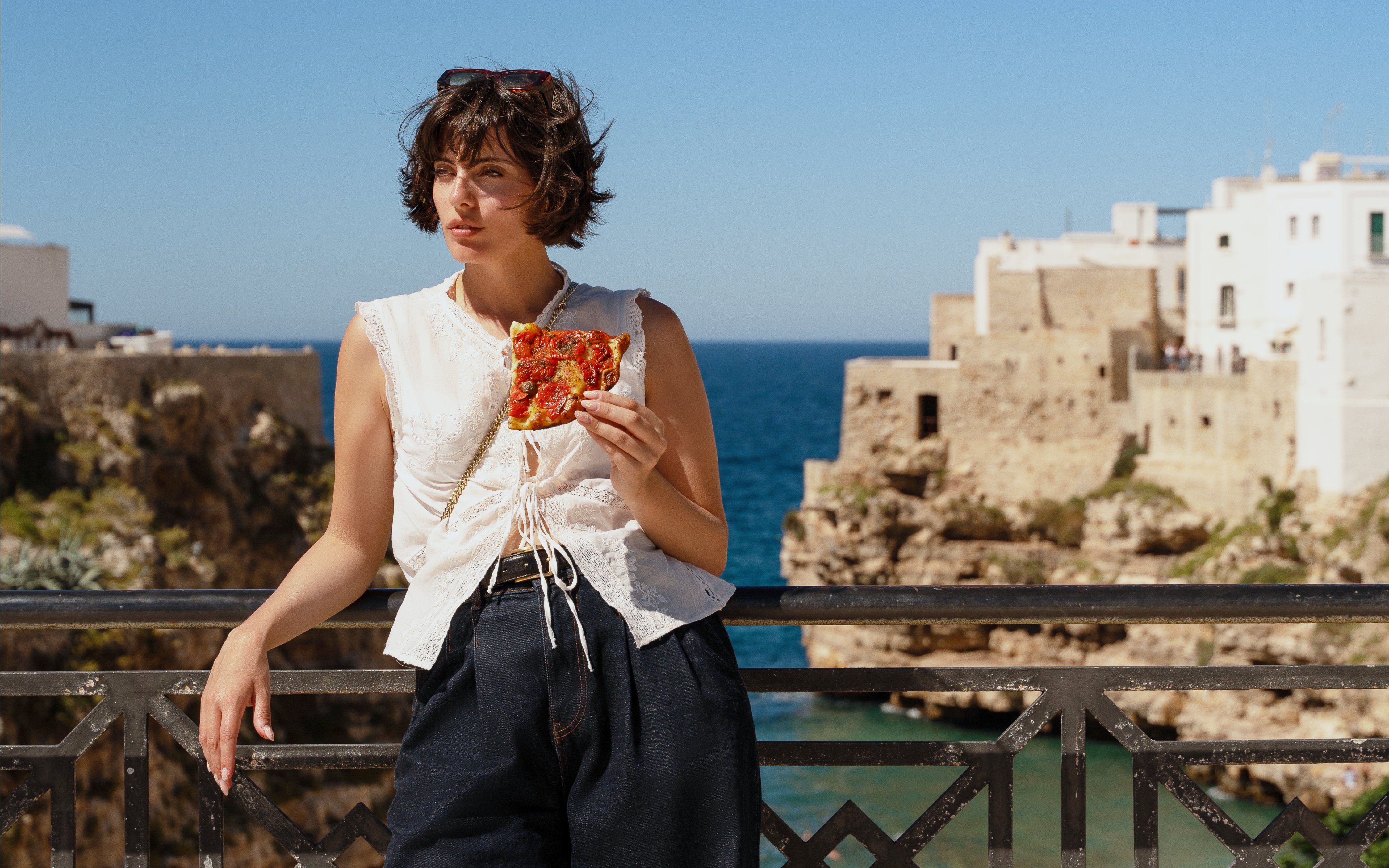 Tourist enjoying pizza with a view of Polignano a Mare coastline.