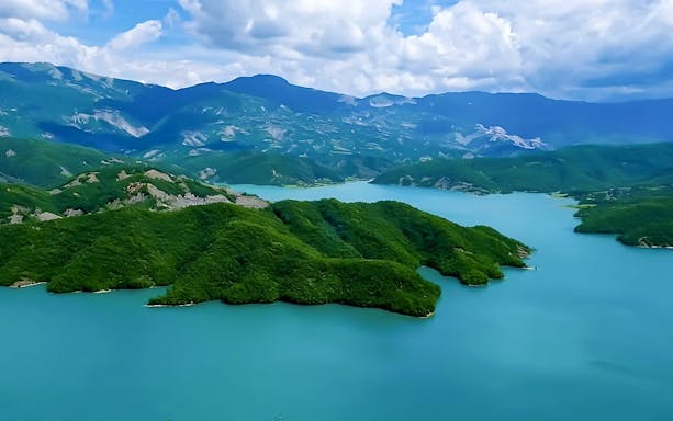Bovilla Lake surrounded by lush green hills and distant mountains.