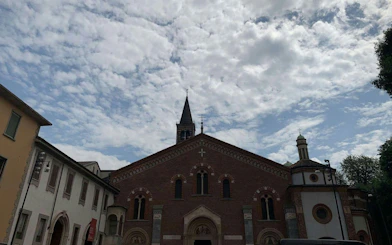 Brick church facade with bell tower under cloudy sky in Milan's Navigli district.