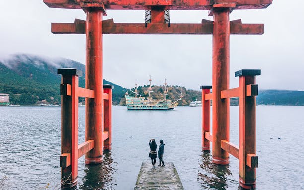 Torii gate overlooking Lake Ashi with a sightseeing ship in Japan.