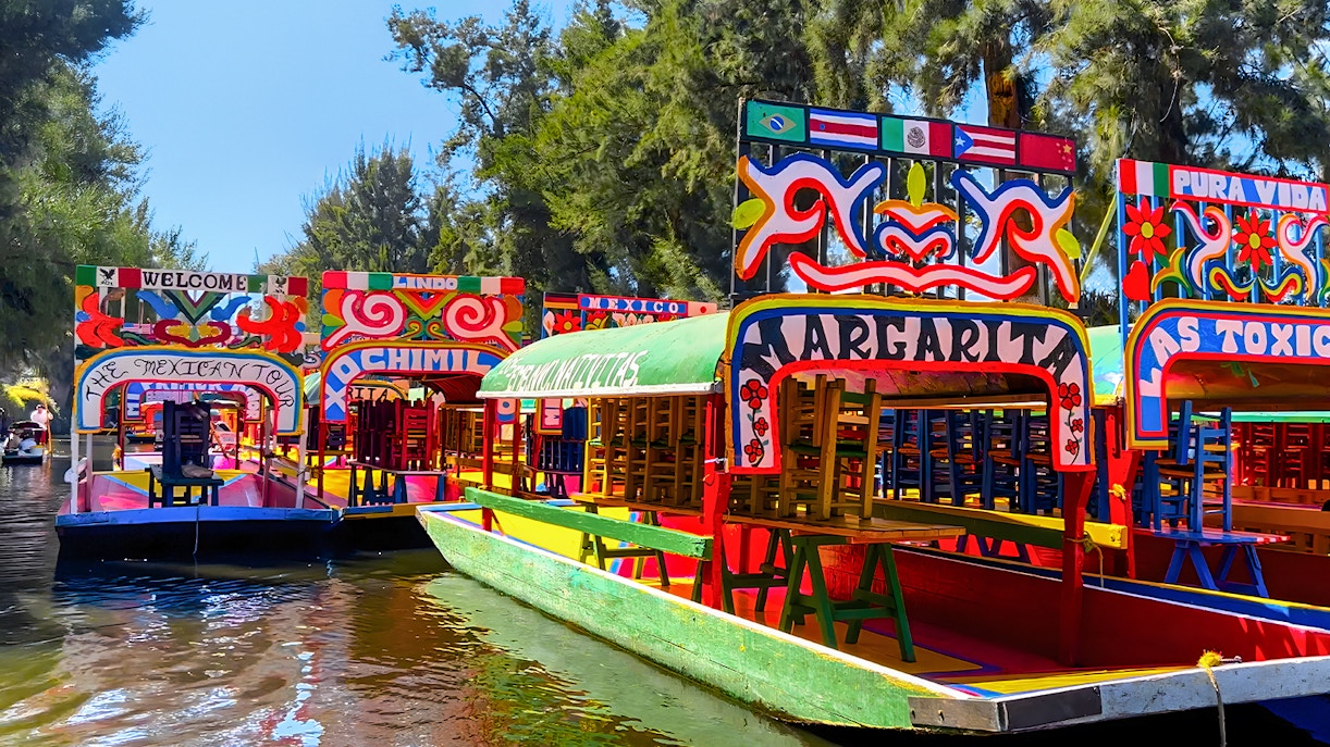 Colorful trajinera boats on Xochimilco canal, Mexico City, with tourists enjoying a guided tour.