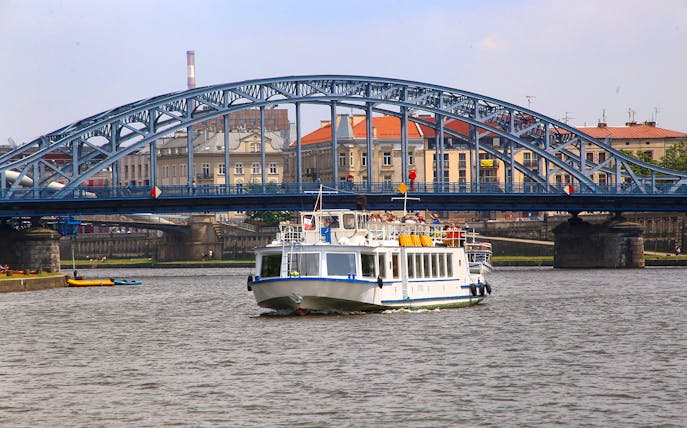 Cruise boat on Vistula River near Krakow with bridge and cityscape in background.