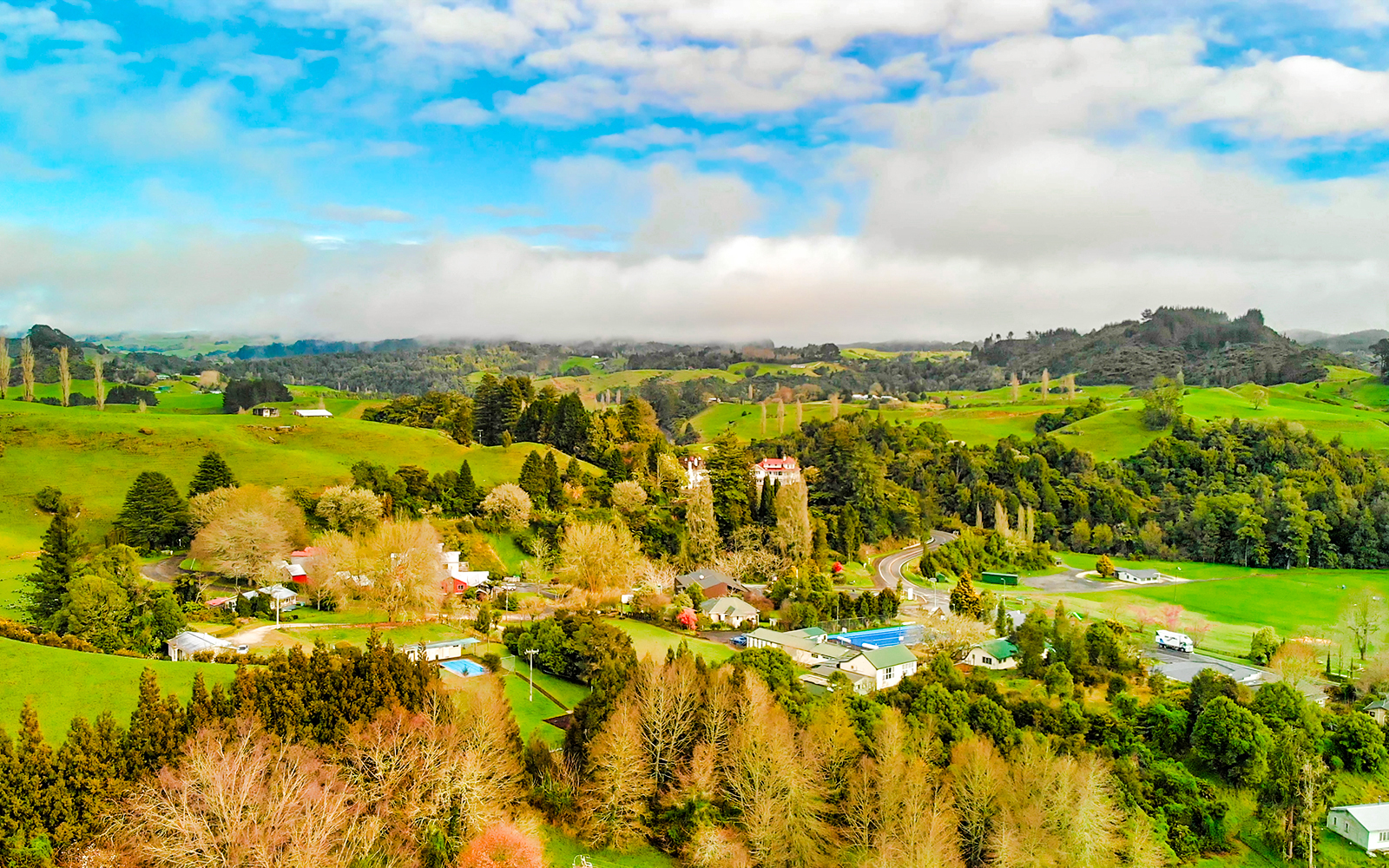 Aerial view of lush green landscape and rural homes in Waitomo, New Zealand.