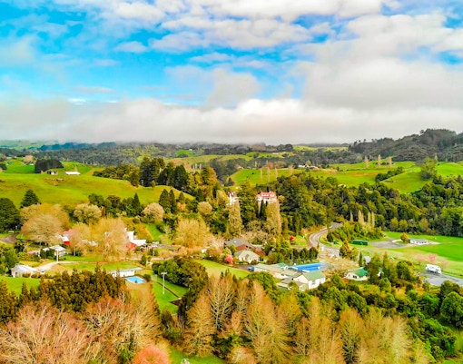 Aerial view of lush green landscape and rural homes in Waitomo, New Zealand.